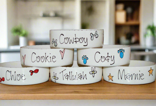Stack of white pet bowls with names and symbols on a gray background