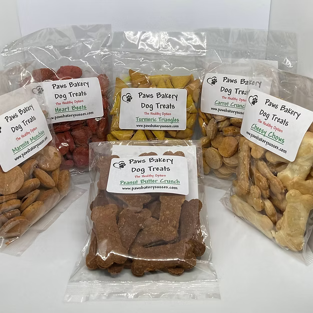 Assorted dog treats in clear packaging with 'Paws Bakery' labels on a white background