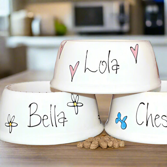 Three white pet bowls with names 'Lola', 'Bella', and 'Ches' on a kitchen counter.
